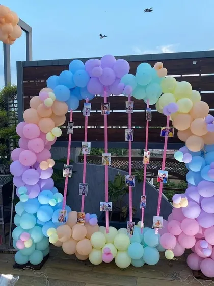 A pastel-themed balloon arch perfect for a daytime celebration on a terrace. This setup also features hanging photo displays, allowing for a personalized touch to the party decor.