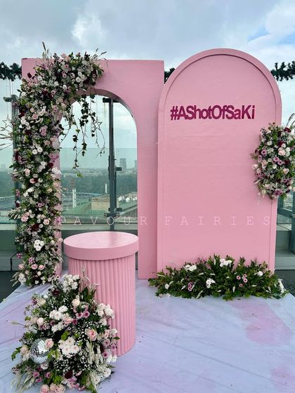 A pretty in pink pre-wedding party setup against a stunning city view. This rooftop decor features a modern arched backdrop with the couple's hashtag and a beautiful floral arch for a chic celebration.