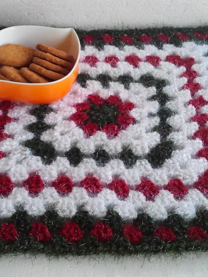 A larger granny square can be used as a placemat or a small decorative mat. This one uses a lovely combination of red, white, and a sparkly dark green yarn.