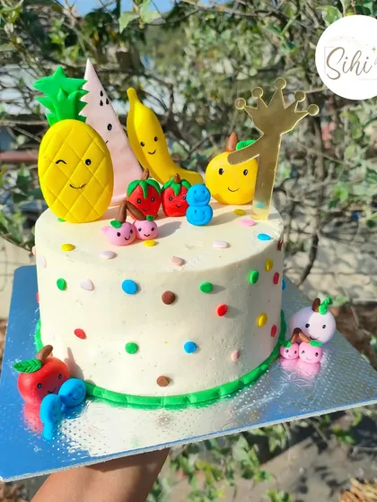 A fruity punch of cuteness. This cake is decorated with adorable, smiling fruit characters made from fondant, including a pineapple, banana, and apple.