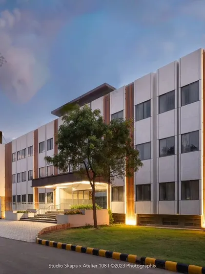 The facade of Jindal Public School at dusk, a project providing free education in rural Bangalore. The design uses earth-toned vertical rafters to break the monotony of the textured grey exterior, which also cleverly conceal service ducts and integrate lighting, creating a timeless and sophisticated institutional building.