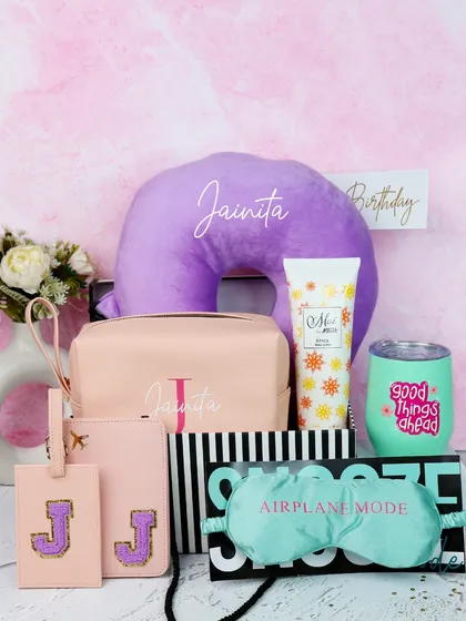 A complete birthday travel hamper. This set includes a personalized neck pillow, utility pouch, luggage tags, eye mask, and a "Good Things Ahead" tumbler.
