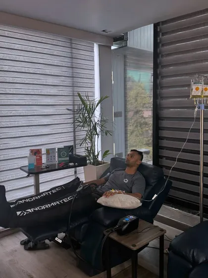 A member recovering in our lounge with Normatec compression boots and an IV drip. We offer advanced recovery options to support your training.