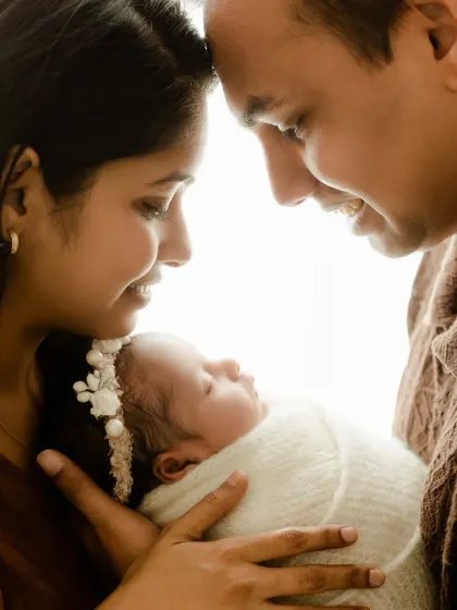 A backlit close-up of a new family. The parents' faces are close together as they hold their baby, creating a glowing, intimate portrait.
