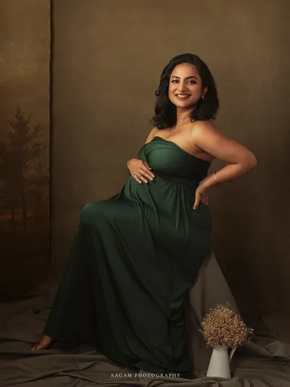 Seated gracefully, this mother-to-be looks completely at ease. The composition, with the simple vase of dried flowers, adds a rustic and earthy touch.