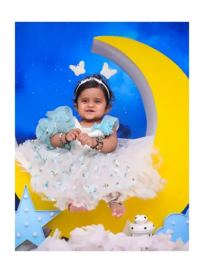 A happy baby girl sits on a crescent moon prop against a starry night sky. Her butterfly headband and joyful smile make this a truly magical and dreamy first birthday portrait.