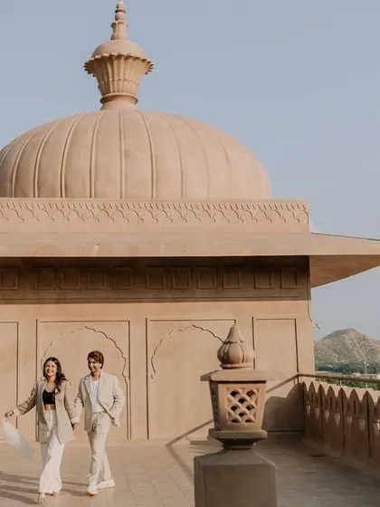 A candid walking shot on a rooftop in Jaipur, with the Aravalli hills in the distance. This photo captures the couple's natural interaction and the grand scale of their destination photoshoot location.