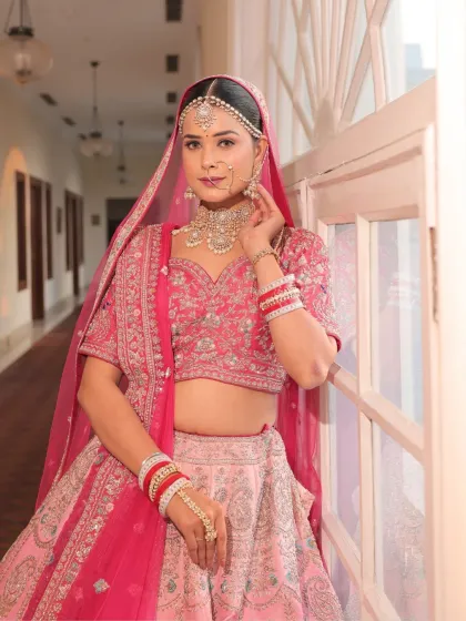 A classic portrait of the bride by the window. The natural light beautifully highlights her soft, luminous makeup and the details of her pink pastel lehenga.