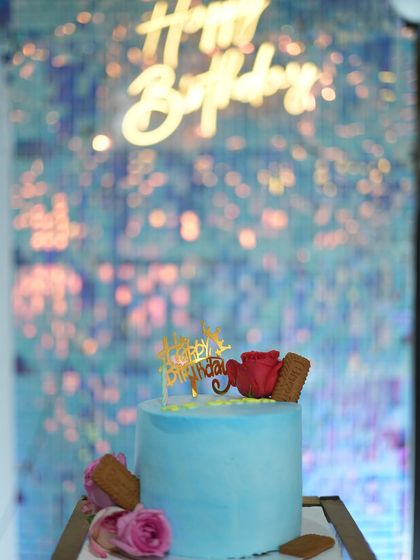 The birthday cake is always a centerpiece. This simple yet elegant blue cake is perfectly complemented by the shimmering, iridescent backdrop and neon sign.