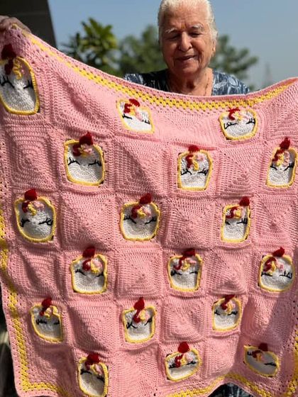 Dadi holding a charming pink blanket adorned with little crocheted chickens. It's a whimsical and unique design that's sure to bring smiles.