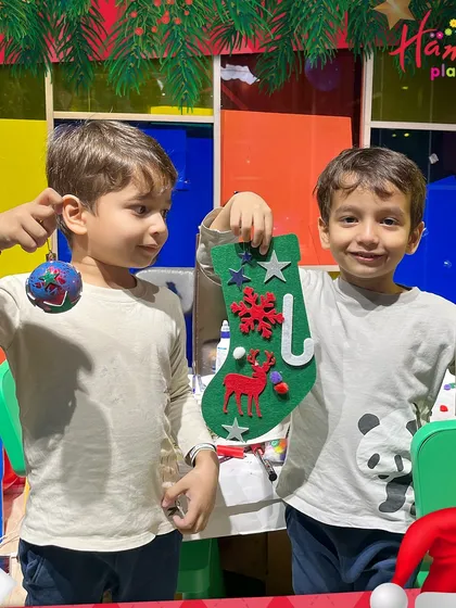 Two boys proudly hold up their finished Christmas crafts: a personalized bauble and a decorated felt stocking. They make the perfect festive keepsakes!