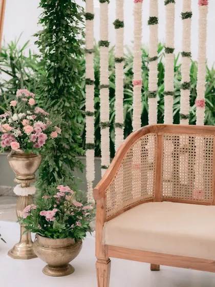 A detail shot of the engagement decor, showing the elegant cane sofa, brass urlis filled with pink flowers, and the beautiful backdrop of hanging white tuberose garlands.