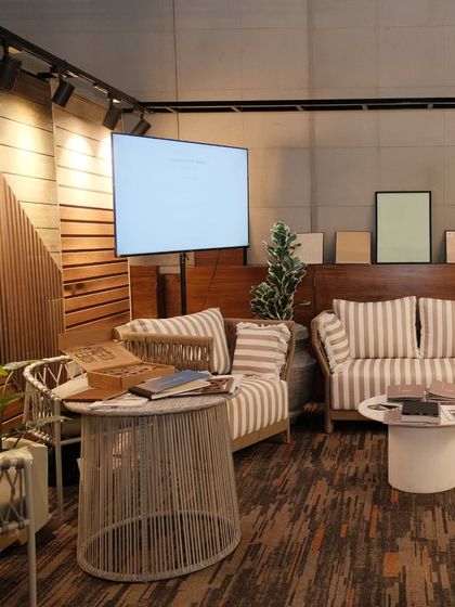 Another view of our booth, showing a lounge area setup with our outdoor furniture, wood-paneled walls, and a display screen for showcasing our projects.