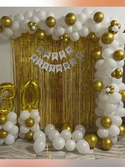 A classic 30th birthday decoration with a white and gold balloon arch and number balloons.