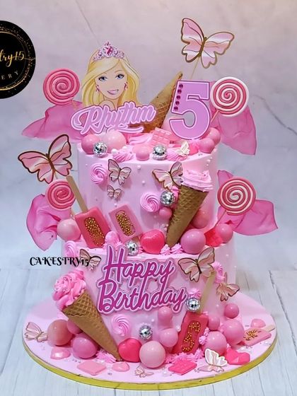 A vibrant two-tier Barbie-themed cake for a 5th birthday. This all-pink creation is loaded with fondant ice cream cones, lollipops, and butterflies for a fun and sweet celebration.