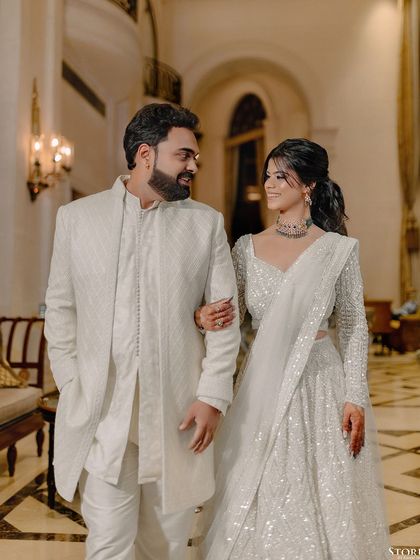 Akanksha and Praneet in a classic portrait, walking arm-in-arm through an elegant hotel corridor.