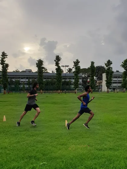 Two athletes stride for stride during a training run on the grass field, building endurance together.