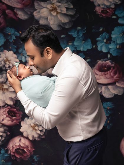 A proud father holds his newborn daughter. The soft lighting and his gentle expression create a warm and loving portrait.