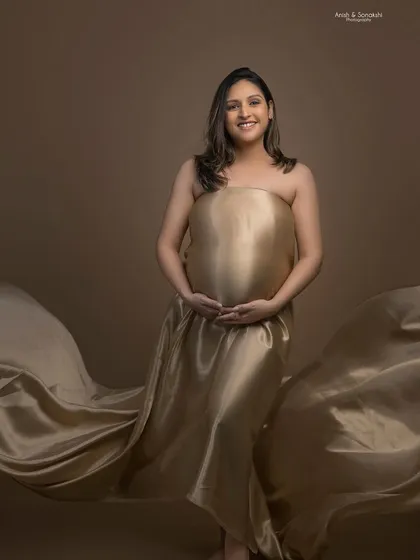 A stunning maternity portrait featuring a flowing golden satin drape. The makeup is kept soft and subtle to focus on the natural beauty and glow of motherhood.