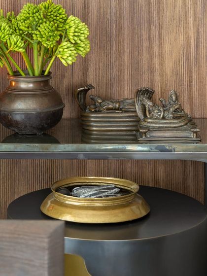 A detail of a console arrangement, featuring antique bronze deities and fresh green florals in a rustic vessel. This juxtaposition of the sacred and the natural, the old and the new, is a hallmark of our styling approach.