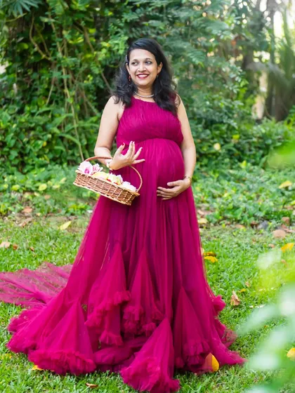 A solo portrait of the mom-to-be, looking radiant in a ruffled magenta gown, holding a basket of flowers in a sunlit garden.