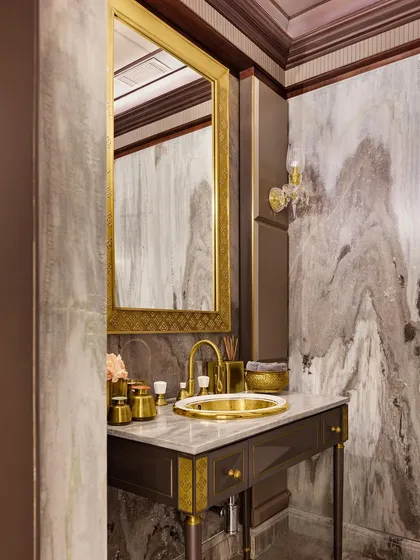 We believe every space deserves meticulous attention. This powder room is a testament to that, featuring captivating book-matched stone and opulent brass fixtures to create a small sanctuary of regal allure and timeless elegance.