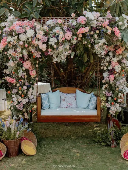 A beautiful wooden swing adorned with a massive arch of pastel pink and white flowers, creating a romantic and picturesque seating area for the couple.