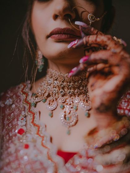 A detail-rich shot focusing on the bride's lips, chin, and stunning choker necklace, with her henna-covered hand adding to the composition.