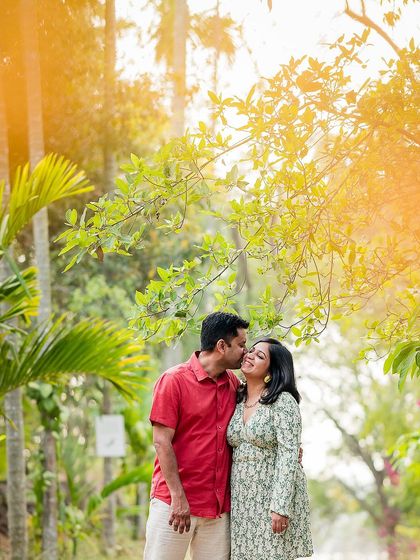 A romantic, sun-kissed photo of a couple sharing a sweet kiss amidst lush greenery. The warm light adds a touch of magic to the moment.