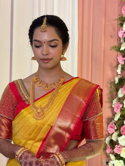 A beautiful portrait of my bride Dr. Sushmita for her Muhurtham in Karur. Her makeup is subtle and elegant, with soft, neutral eyeshadow and a natural lip tint that enhances her features, perfectly matching her classic yellow and red saree.