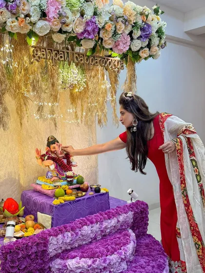 A candid moment of prayer in front of the purple and pastel floral Ganpati decor. This design creates a warm and inviting space for devotion and celebration.
