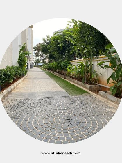 The driveway at Saritha Splendor features a combination of paving patterns, including a circular cobblestone detail. The edges are softened with a mix of lawn and planted beds, making a functional space more aesthetically pleasing.