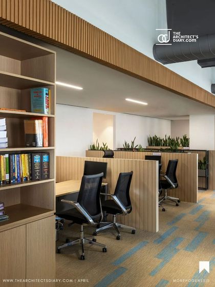 The open-plan work area at Adani Realty is organized with low wooden partitions and integrated shelving. This approach defines individual zones without sacrificing the sense of community and open communication.