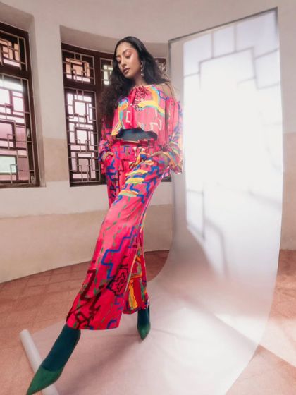 A full-length view of the bell-sleeve top and matching trousers from Advait. We paired this vibrant look with bold green sock boots to create a cohesive, color-blocked effect that is central to this fashion story.