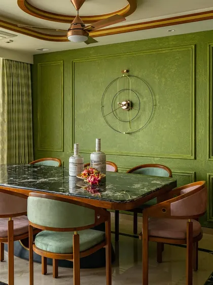 A view of the dining room, where olive green walls with classical Victorian-style molding create a timeless charm. The custom clock and teakwood furniture add to the elegant blend of styles.