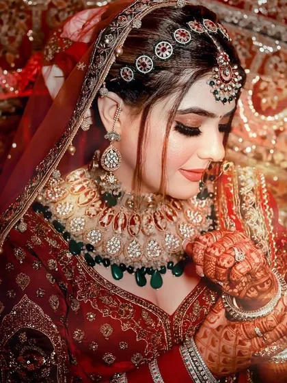 A stunning bridal portrait. The heavy polki necklace with green and red stones, paired with a statement matha patti, creates a look of pure opulence.
