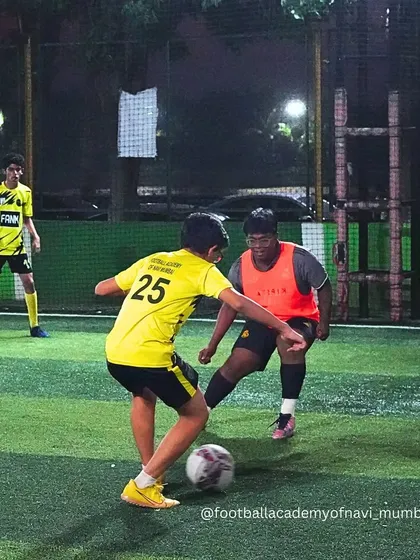 A player in a yellow bib skillfully maneuvers the ball around a defender in an orange bib.