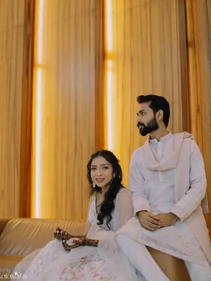 A posed portrait with a modern, minimalist background. The clean lines of the wood paneling contrast beautifully with their traditional attire.