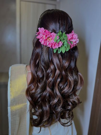 A detailed shot of the bridal hairstyle, featuring soft waves and a beautiful pink floral accessory that adds a touch of modern romance to the traditional look.