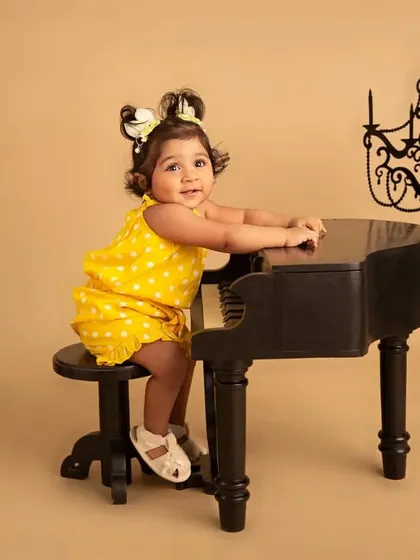 A mini maestro at her piano. This adorable toddler portrait features a little girl in a bright yellow outfit playing on a miniature grand piano, a classic and charming setup.