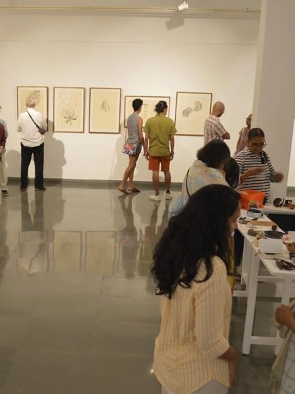 Visitors at the preview of 'Bring me Flowers', observing both the wall-hung works and the table installations.