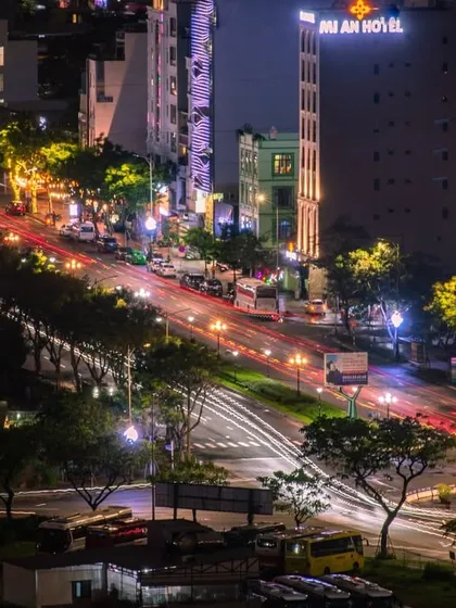 A long-exposure shot of a busy street in Vietnam at night, with red and white light trails from traffic flowing through the city.