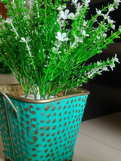 This turquoise metal planter has a lovely hammered texture with gold accents. It's styled with delicate white artificial flowers, creating a rustic and pretty tabletop piece.