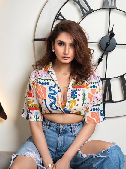 A casual yet striking portrait of Ragini Dwivedi. This shot combines a playful shirt with ripped jeans, showcasing a different, more relaxed side of her personality.