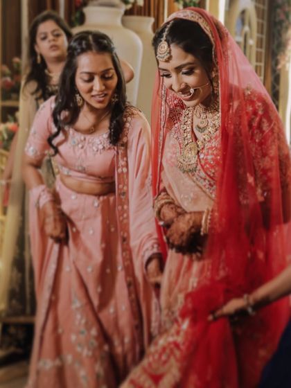 A bride shares a quiet moment with her bridesmaid, who helps her with her lehenga. These small acts of support are a big part of the wedding story.