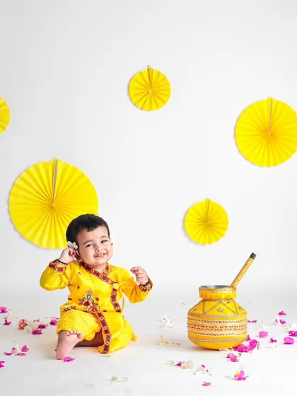 A minimalist Janmashtami setup with a clean white background. The yellow paper fans and scattered petals add a pop of color while keeping the focus on this sweet baby Krishna.