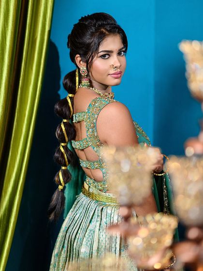 A detailed view of a modern bubble braid hairstyle, perfect for an engagement or sangeet. The shot also showcases the intricate design of the back of the blouse.