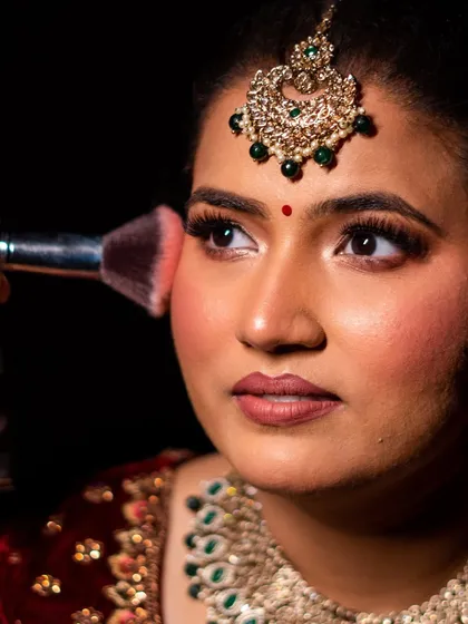 A close-up shot during the makeup application. This image captures the moment of adding a touch of blush to create that perfect bridal glow.