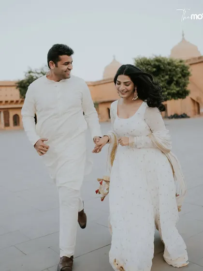 A playful, candid moment of the couple running and laughing in a Jaipur palace courtyard. Their all-white outfits and genuine smiles create a fresh, joyful, and authentic pre-wedding photograph.