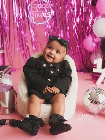 A happy baby girl enjoying her half-birthday celebration, surrounded by pink and black balloons and a "Good Times" neon sign.